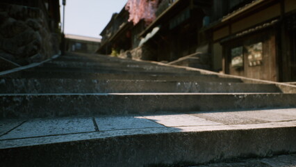 Visitors walk up weathered stone steps in an old town, surrounded by historic buildings. Cherry blossoms bloom nearby, hinting at the gentle arrival of spring and peace.