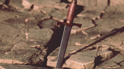 Fototapeta premium At the heart of a large cracked stone, a gleaming sword stands upright. The sunlight glints off its blade, while the rugged terrain tells tales of ancient battles and heroic legends.