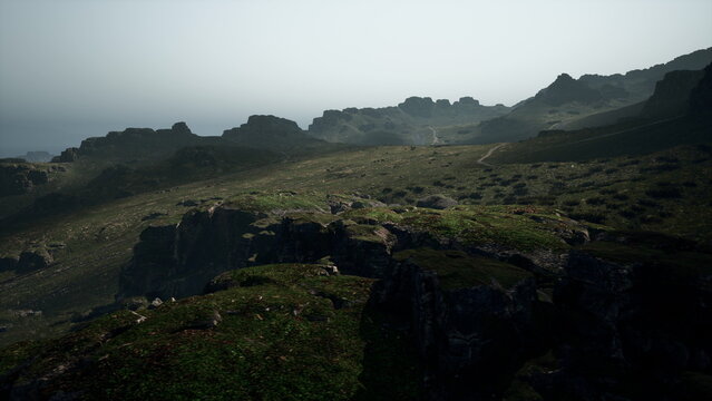 Sunset casts a soft glow over rugged hills by the coast. The landscape reveals rocky cliffs, lush green patches, and winding paths that lead to the endless horizon over the ocean.