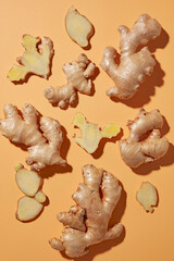 Flat lay of ginger roots and lemon slices scattered naturally on orange background. Minimal scene supports concepts of organic food photography and wellness ingredients