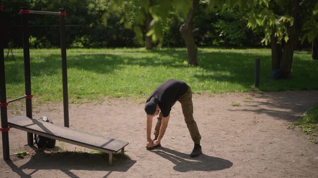 White Man Doing Forward Bends And Toe Touches At Outdoor Training Area, Checking Flexibility And Range, Slow Controlled Motions, Park Bench And Bars In Background, Focused Preparation