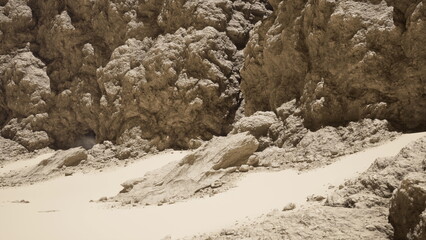 Adventurers navigate a harsh landscape filled with rough, textured rocks and smooth sandy areas. Bright sunlight casts shadows, creating a striking contrast in this remote location.