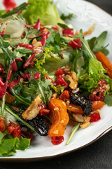 Fresh mixed salad with greens, roasted vegetables, nuts and berry dressing served on a white plate