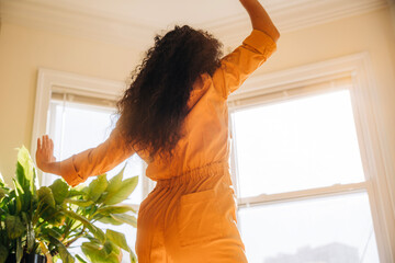 Person in orange jumpsuit poses gracefully in bright sunlit room