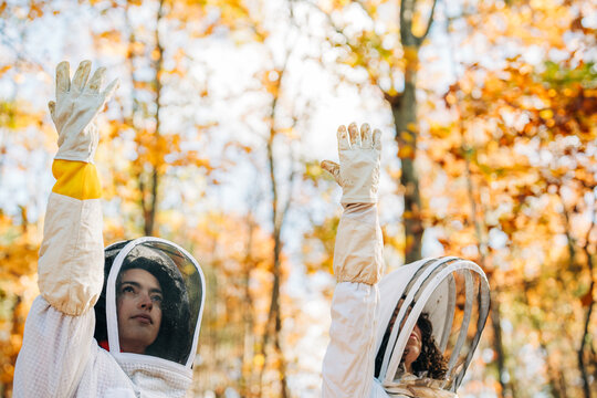 Two beekeepers raise gloved hands amid vibrant autumn trees
