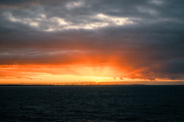 Fiery sunset over Baltic sea with clouds and distant wind turbines