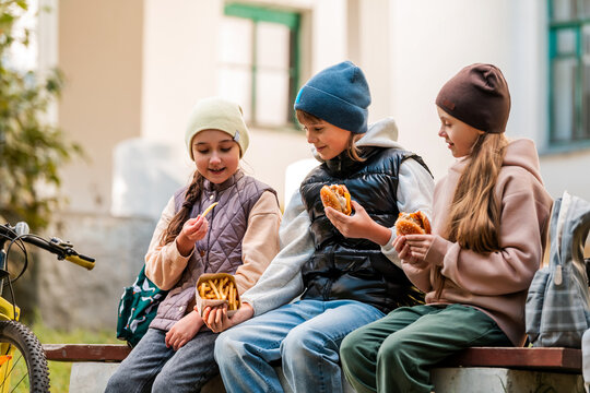 Three girls enjoying fast food outdoors. Friends sharing meal.