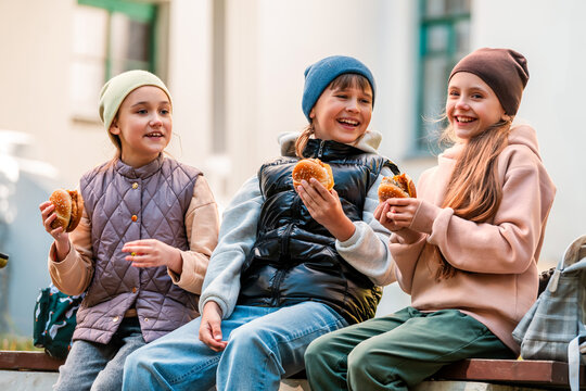 Three girls enjoying fast food outdoors. Friends sharing meal.