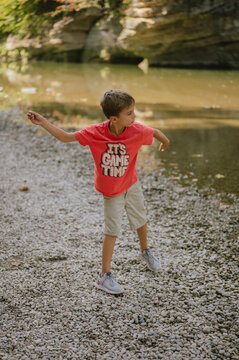 Young boy skips rocks along pebbled creek shore in nature
