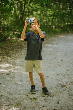 Young boy uses toy camera while exploring forest trail