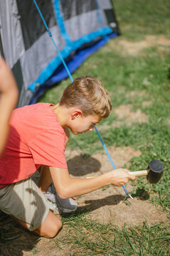 Young boy hammers tent stake into ground on sunny day