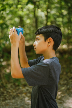 Young diverse boy takes photo with toy camera on forest trail
