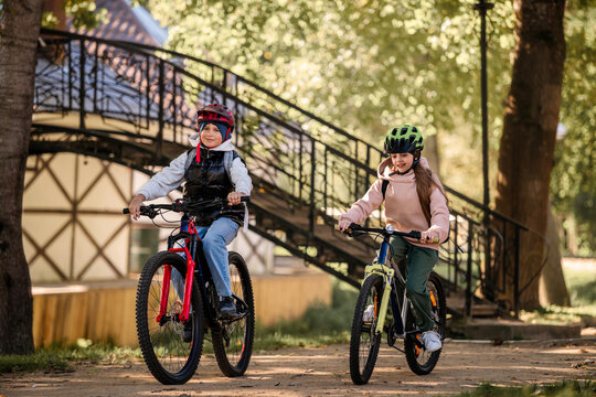 Two happy kids in helmet on bicycle looking at camera in park.