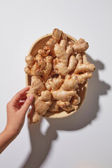 Flat lay with a hand holding ginger roots against a clean background. Natural raw herbal ingredients and natural health themes