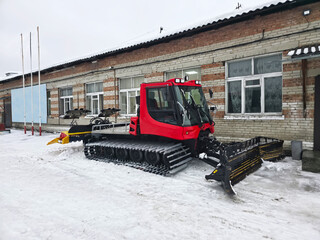 Red snow sealing machine with a snowmobile and a ski trail groomer. Specialized winter equipment for mountain resorts and outdoor activities.