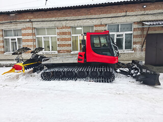 Red snow sealing machine with a snowmobile and a ski trail groomer. Specialized winter equipment for mountain resorts and outdoor activities.