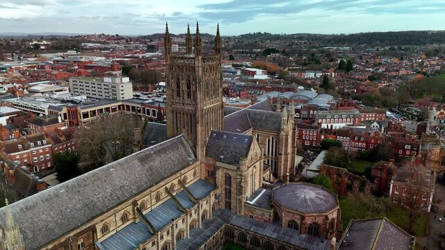 Dramatic aerial dolly back from the detailed Worcester Cathedral facade, revealing the full historic landmark and tracking over the adjacent River Severn in Worcestershire, UK.