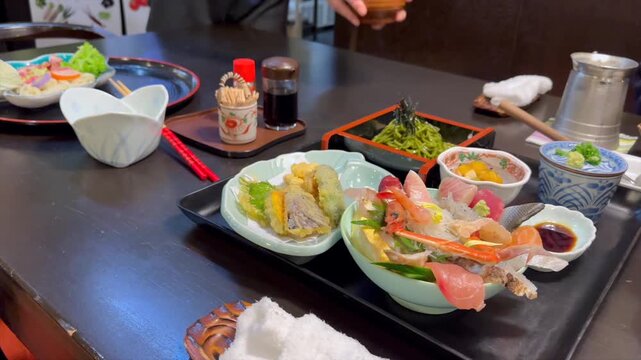 Gliding camera view of a traditional Japanese kaiseki meal showcases sashimi tempura and side dishes, revealing a warm spread with nabe simmering gently at table