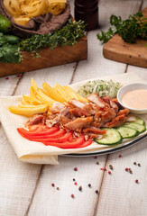 Doner plate with sliced chicken fries fresh vegetables and sauce served on lavash in rustic restaurant style