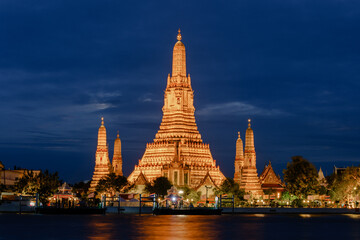 Fototapeta premium Magnificent wat arun illuminated at night against the serene river in bangkok, thailand