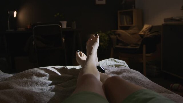 POV of woman with bare feet, wearing house arrest ankle bracelet, lying in bed with crossed legs