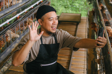 Happy Farmer Waving During Video Call in His Chicken Coop © Gatot