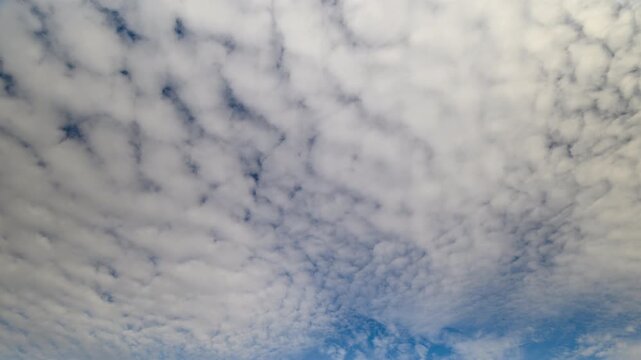Wide textured cloudscape with blue sky, rippling altocumulus layers creating mosaic pattern, soft sunlight highlighting contours, expansive aerial perspective above distant horizon