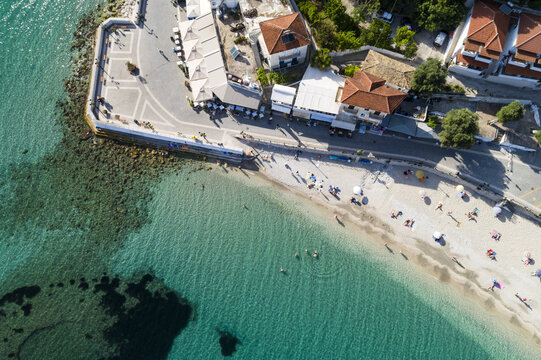 Aerial view of the coastline where turquoise waters meet the sandy beach, contrasting with the red-tiled roofs of buildings along the coast, Panagia, Thasos Regional Unit, Greece.