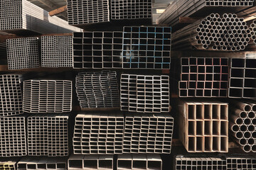 Close-up of stacked square steel hollow section profiles and round steel pipes with visible cut ends stored inside an industrial metal warehouse