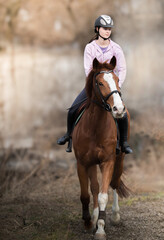 A young girl riding a chestnut horse in rural countryside.