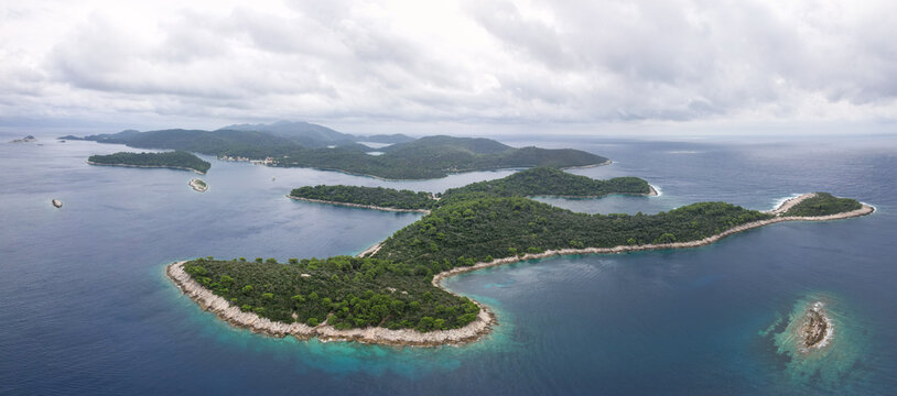 Aerial view of a stunning archipelago where emerald forests meet the deep blue Adriatic Sea under a vast, cloudy sky, Pomena, Dubrovnik-Neretva County, Croatia.