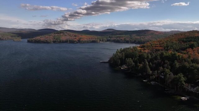 Aerial view of a tranquil lake reflecting the sky, bordered by lush forests with autumn foliage, creating a scenic contrast, Alton, New Hampshire, United States.