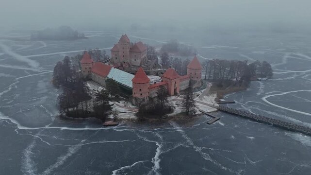 Aerial view of the red brick Trakai Island Castle on a small island surrounded by a frozen lake with cracked ice patterns, Trakai, Lithuania.