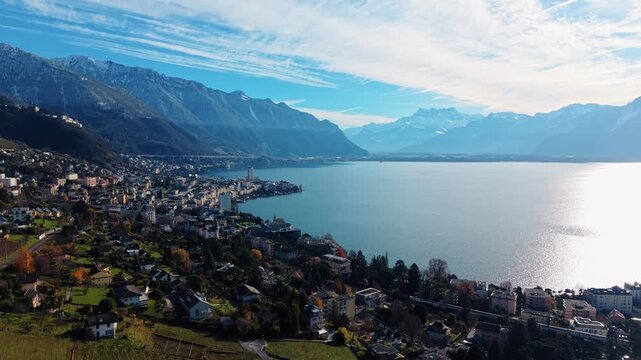 Aerial view of the cityscape of Montreux along the lake, nestled against snow-capped mountains under a bright blue sky, Vaud, Switzerland.