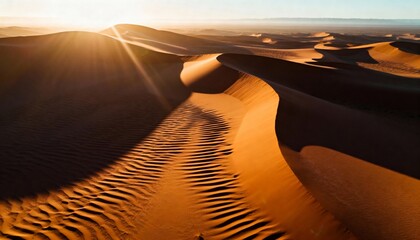 Majestic desert sand dunes bathed in golden light during sunrise, creating dramatic shadows and intricate rippled patterns. A breathtaking aerial view highlighting the vast, arid landscape for trav...