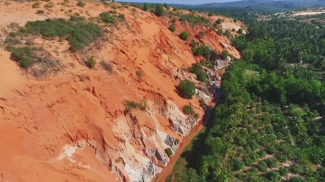 Aerial view of the Fairy Stream in Mui Ne: striking red sandstone formations and lush green jungle under a clear blue sky.