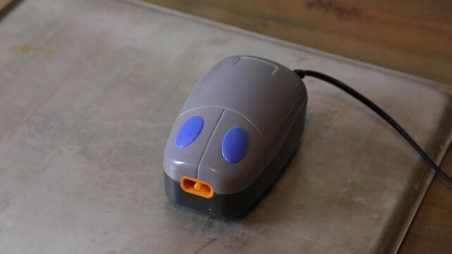 Gray aquarium air pump with blue buttons and orange output nozzle. Small, compact oxygenator for fish tank filtration system.