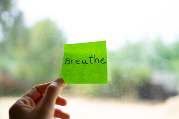 Hand holding green sticky note with breathe written on it by window