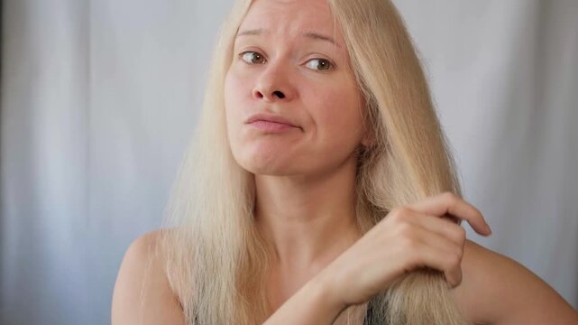 Beautiful woman with messed up hair. Unhappy grimacing face. Blond bleaching hairstyle with problem brittle hair. Split ends of bleached hair. Hairstyle, daily beauty routine. Cosmetic and trichology