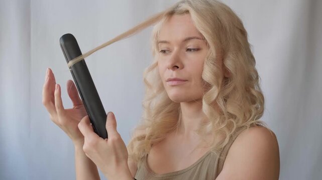 Beauty close-up of blonde woman looks focused and confident, preparing for hair curl styling. Curly hairstyle process, female daily beauty routine and self-assurance. Calm face express control