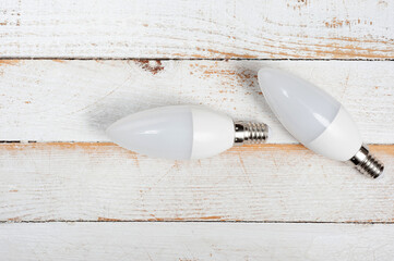 Two LED lamps with E14 sockets lying on a wooden surface.