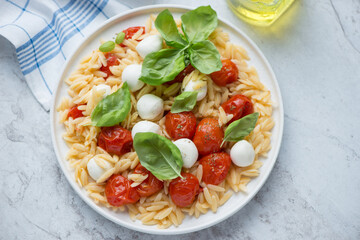 Plate of caprese pasta salad with orzo on a white stone background, horizontal shot, high angle view