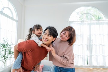 Family enjoys time together in living room with child on parent's back and smiling at each other