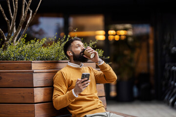 Portrait of businessman using phone while drinking coffee on a coffee break on a city street.