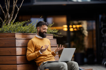 Portrait of a businessman sitting on a bench outdoors and having conference call on laptop.