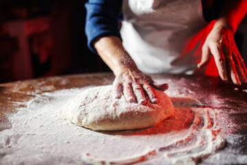 Hands kneading bread dough on wooden table