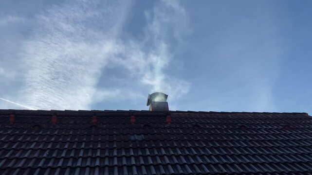 Minimalistische Au&szlig;enaufnahme eines geneigten Hausdachs mit Dachziegeln, Schornstein und Dachfenster vor blauem Himmel mit leichten Wolken. Klare Linien und reduzierte Bildgestaltung machen das Motiv 