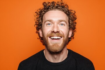 Fototapeta premium Joyful young man with curly hair smiling against bright orange background while enjoying a carefree moment with contagious energy and happiness, ideal for uplifting imagery