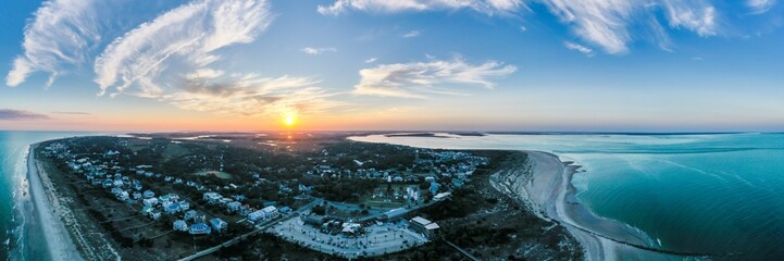Aerial view of the golden sun setting over the tranquil waters and sandy shores of Tybee Island, with charming houses nestled amidst the greenery, Tybee Island, Georgia, United States.