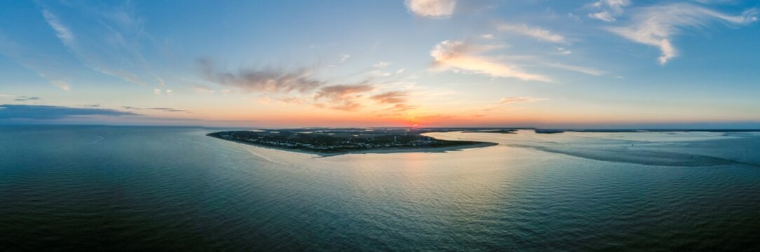 Aerial view of the sun dips below the horizon, casting a golden glow over the tranquil waters surrounding the serene shores of Tybee Island, Georgia, United States.